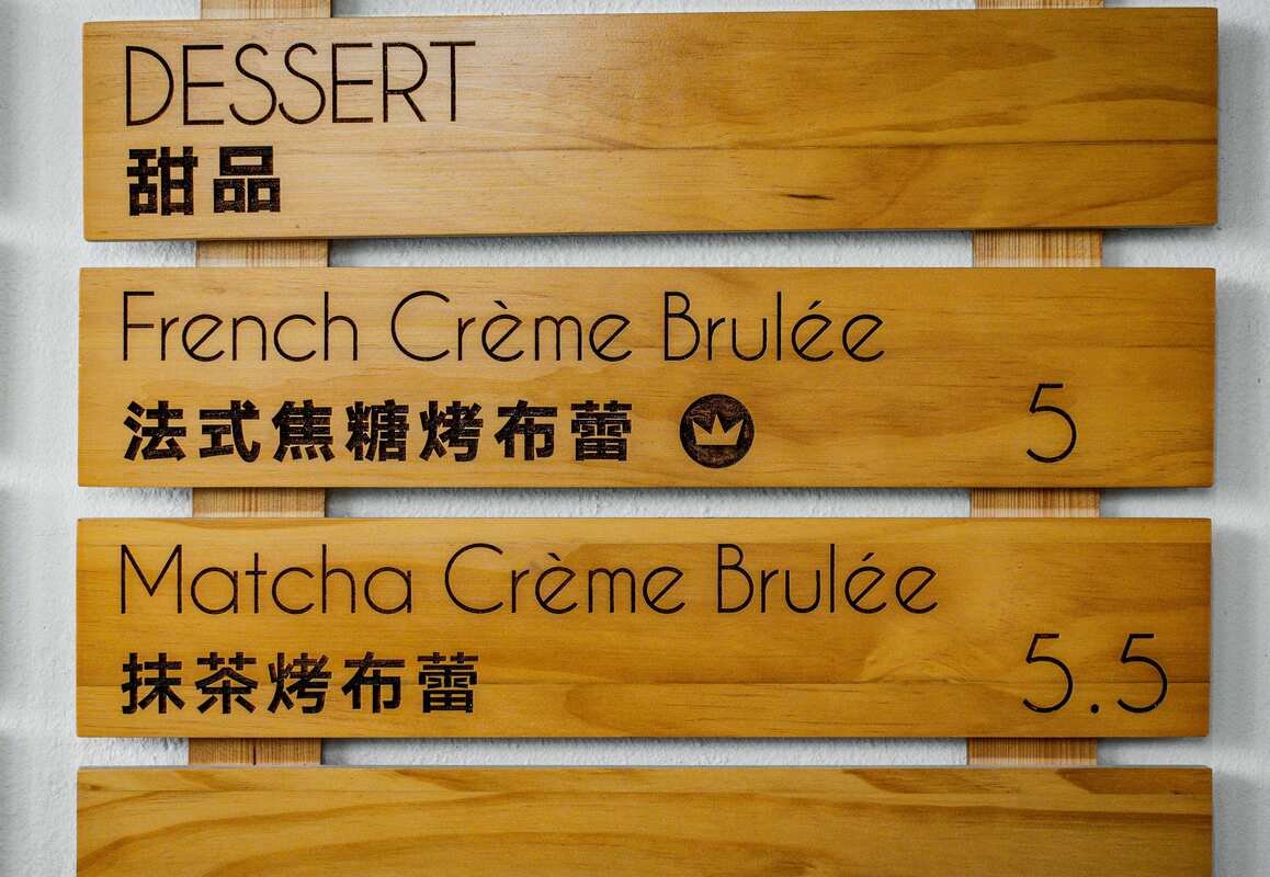 Wooden dessert menu displaying French Crème Brulée and Matcha Crème Brulée with English and Chinese translations