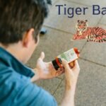 A person holding a bottle of ointment while examining its label, with "Tiger Balm" written above and an illustration of a tiger beside it