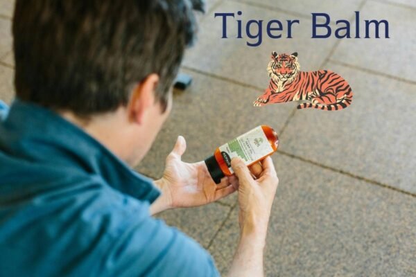 A person holding a bottle of ointment while examining its label, with "Tiger Balm" written above and an illustration of a tiger beside it